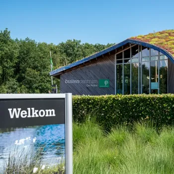 Buitencentrum De Pelen met informatiebord en groen dak, omringd door natuur.