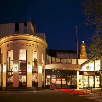 Munttheater in Weert bij avond met verlichte entree, rode loper en de Martinustoren op de achtergrond.