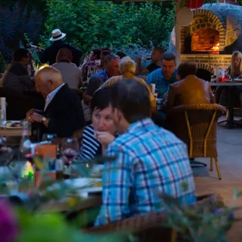 Terras van Restaurant Diverso in Nederweert met gasten die dineren bij een houtoven, omringd door groen en warme verlichting.