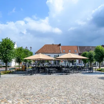 Terras van Grand-Café ’t Aod Kloaster op een plein in Stevensweert, met tafels, parasols en historische bebouwing op de achtergrond.