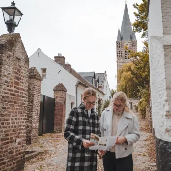 Twee wandelaars bekijken een routekaart in een straatje in Thorn, met de kerktoren op de achtergrond